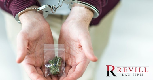 hands with handcuffs holding a small bag of marijuana